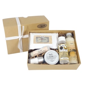 May include: A brown gift box with a white ribbon contains a set of bath and body products. The products include a bar of soap, a lip balm, a bottle of dry oil spray, a jar of shea butter, and a bag of mineral salts. The products are all labeled with the brand name "Sweet P".