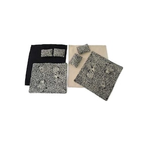 May include: A collection of home textiles, including a black bedspread with two matching pillows, a beige bedspread with two matching pillows, and two leopard print placemats. The leopard print has black and tan spots.