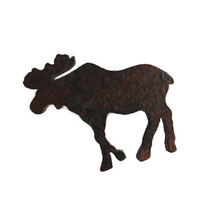 May include: A rusty brown metal moose silhouette, cut out with antlers and four legs, stands against a white background. The moose is facing left, with a textured surface and a rustic appearance.