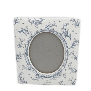May include: A square picture frame with a white base and a blue floral pattern featuring stylized tulips and vines. The frame has a central oval opening with a gray backing. The design is consistent across the entire surface of the frame.