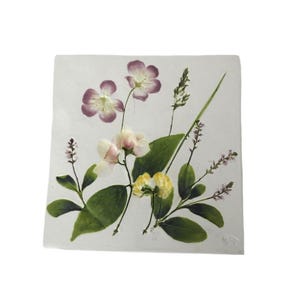 May include: A square white ceramic tile featuring a botanical illustration of various wildflowers and green leaves. The design includes purple, pale pink, and yellow blossoms arranged with slender stems and foliage across the flat surface.