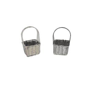May include: Two small, woven baskets with handles. The baskets are gray and black, with a square shape and a handle that arches over the top. The baskets are made of a woven material and are set against a white background.