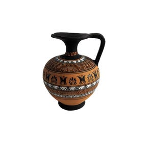 May include: A terracotta-colored ceramic pitcher featuring a black handle, base, and rim. The body is decorated with horizontal bands of black and white geometric patterns, including Greek key motifs and stylized floral elements around the center.