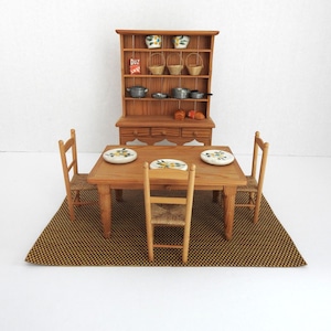 May include: A miniature wooden dining set featuring a rectangular table with three chairs, a hutch with shelves, and various small kitchen accessories. The table is set with three plates, while the hutch displays bowls, baskets, and cookware.