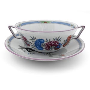 May include: White ceramic soup bowl and saucer set. The bowl has two handles and is decorated with colorful floral patterns in blue, red, and purple. The rim and saucer edge are trimmed with a light purple border.