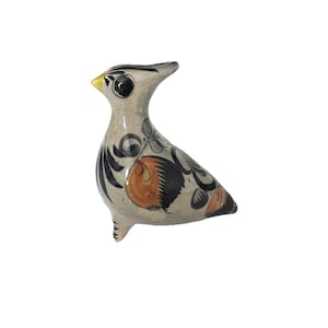 May include: A ceramic bird figurine with a light gray base color. The bird has black, orange, and blue decorative patterns. The beak is yellow. The bird is standing on three small feet.