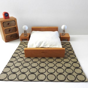 May include: Miniature bedroom set with a wooden bed, nightstands, and a dresser. The bed has a white pillow and is set on a patterned rug. Two small lamps with white globes sit on the nightstands. A red and orange clock sits on the dresser.