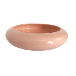 May include: A round, peach-colored ceramic bowl with a smooth, glossy finish. The bowl has a wide, shallow design, perfect for decorative purposes or serving. The interior and exterior are the same color.
