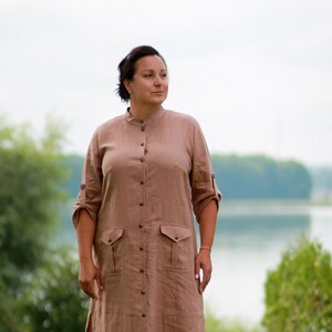 May include: A long, brown linen dress with a button-up front, long sleeves, and two pockets. The dress has a relaxed fit and a slightly flared skirt.