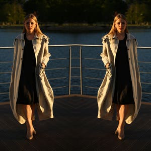 Può includere: Due donne che indossano lunghi cappotti beige con cappuccio sopra abiti neri. Sono in piedi su una piattaforma di legno con una ringhiera dietro di loro.