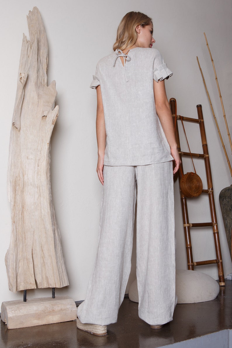 May include: A light gray linen pantsuit with a relaxed fit. The top has a round neckline and short sleeves with ruffles. The pants are wide-legged and have a straight fit.