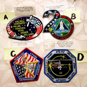 May include: Four embroidered space shuttle mission patches. One patch is oval-shaped with a space shuttle and the names of the crew. Another patch is in the shape of the number 20 with a space shuttle. The other two patches are pentagon and octagon shaped with space shuttle designs.