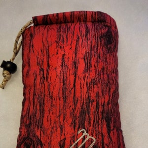 May include: Red drawstring bag with a wood grain pattern and a silver Virgo zodiac symbol.