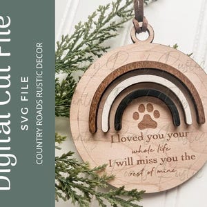 May include: A round wooden ornament featuring a layered rainbow design in dark brown, white, and black. A paw print is engraved above the text: I loved you your whole life, I will miss you the rest of mine. A brown leather cord is attached to the top.