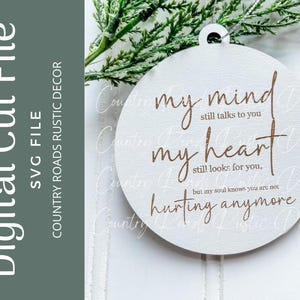 Pode incluir: Um ornamento redondo branco com o texto "my mind still talks to you my heart still looks for you, but my soul knows you are not hurting anymore" em letras marrons.