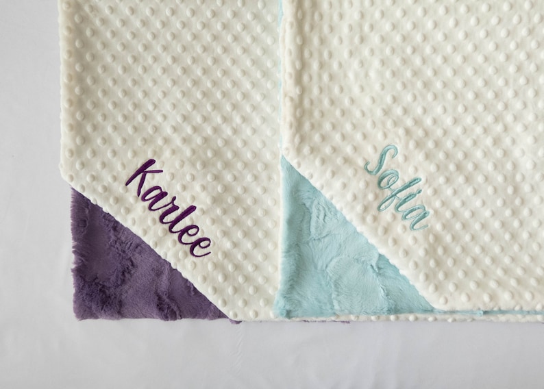 May include: Two white baby blankets with different colored backing. One blanket has the name "Karlee" embroidered in purple and the other has the name "Sofia" embroidered in blue.