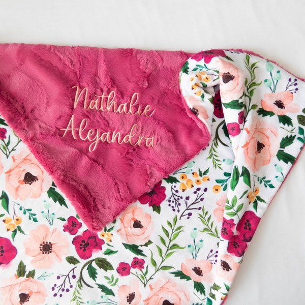 Puede incluir: Una manta de bebé de estampado floral rosa y blanco con un lado rosa suave y afelpado. La manta está personalizada con el nombre "Nathalie Alejandra" bordado en rosa claro.