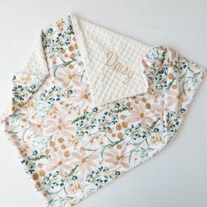May include: A white and pink floral baby blanket with a white minky backing. The blanket is personalised with the name "Daisy" embroidered in gold thread.