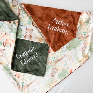 May include: A green and brown baby blanket with a woodland animal print. The blanket has two personalized patches, one with the name "Grayson Edward" and the other with the name "Archer Graham".