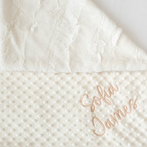 A personalized baby blanket in ivory fluffy minky and ivory dimple dot textured minky.  The name is embroidered on the dimple dot side in a neutral putty color.  Can be customized.