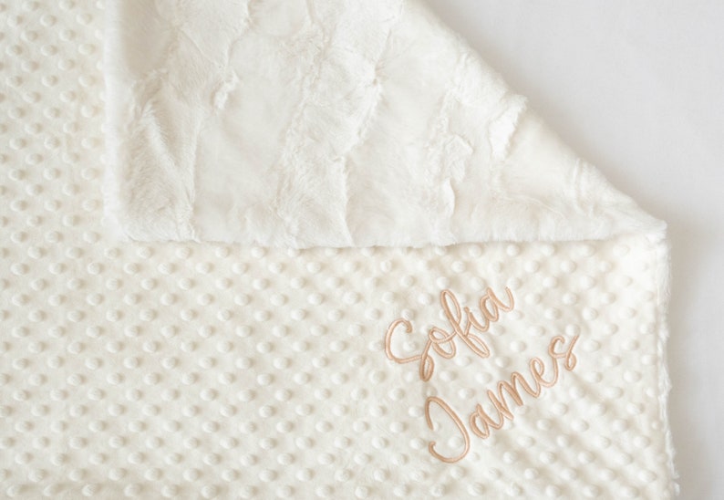 A personalized baby blanket in ivory fluffy minky and ivory dimple dot textured minky.  The name is embroidered on the dimple dot side in a neutral putty color.  Can be customized.