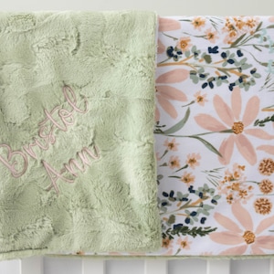 May include: A green plush baby blanket with a floral print on the reverse. The blanket is personalised with the name "Bristol Ann" embroidered in pink thread.