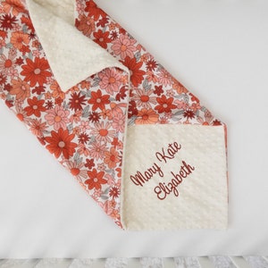 May include: A white and orange floral baby blanket with a soft, white minky backing. The blanket is personalized with the name "Mary Kate Elizabeth" embroidered in red.