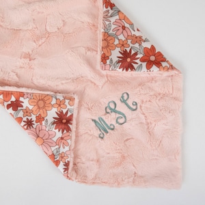 May include: A pink and white baby blanket with a floral pattern on one side and a soft, fuzzy texture on the other. The blanket is personalized with the monogram "MPE" in teal thread.