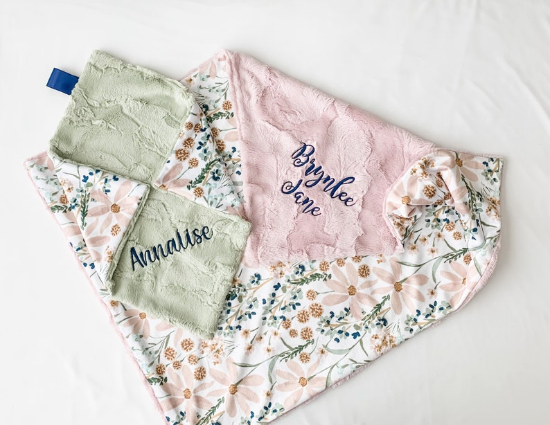 May include: Two personalised baby blankets with floral patterns. One is green with the name Annalise embroidered on it, and the other is pink with the name Brynlee Jane embroidered on it.