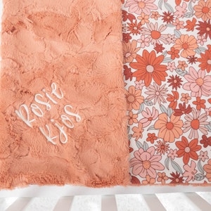 May include: A peach-colored plush blanket with a floral print on one side. The plush side has the name "Rosie" embroidered in white.