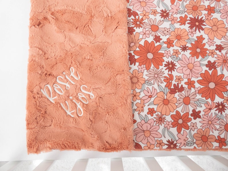 May include: A peach-colored plush blanket with a floral print on one side. The plush side has the name "Rosie" embroidered in white.