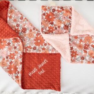 May include: A red and white floral baby blanket with a soft pink minky backing. The blanket is personalized with the name "Mavis-James Gail" in white embroidery.