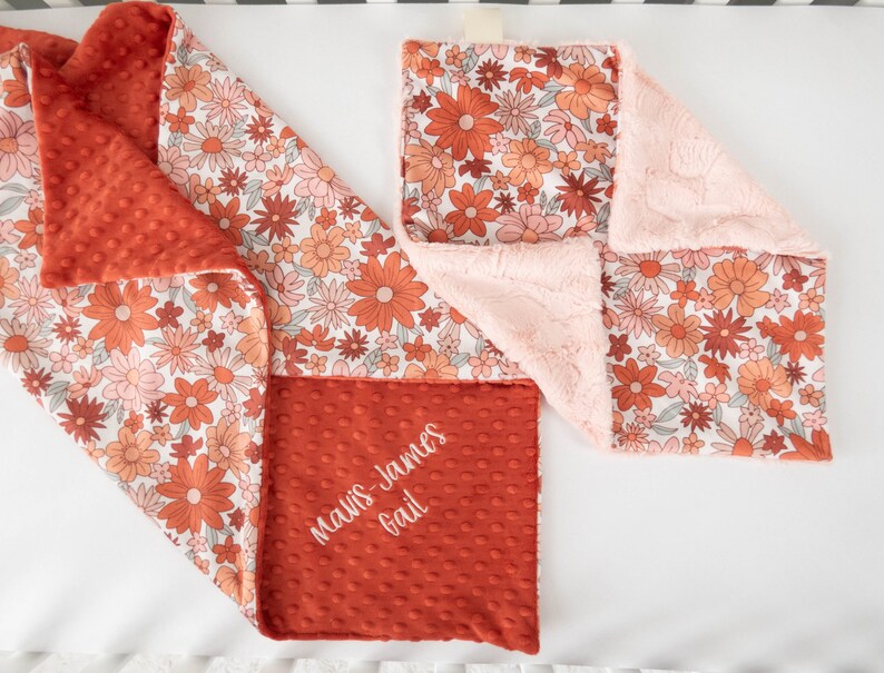 May include: A red and white floral baby blanket with a soft pink minky backing. The blanket is personalized with the name "Mavis-James Gail" in white embroidery.