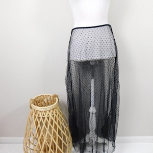 May include: A black sheer skirt with polka dots. The skirt is on a white mannequin and is long, reaching below the knees.