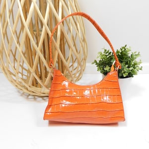 Op de afbeelding: Een feloranje handtas met een krokodil-geprägd ontwerp en een enkele bovenste handgreep.