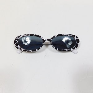 May include: Black and white oval sunglasses with a white frame and black lenses.