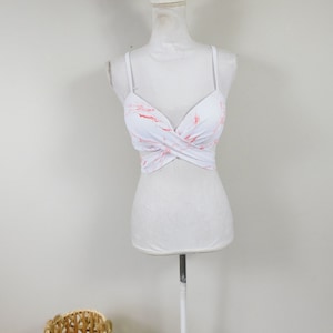 Op de afbeelding: Witte crop top met een rood en wit marmerpatroon. De top heeft een kruislings ontwerp aan de voorkant en dunne bandjes.