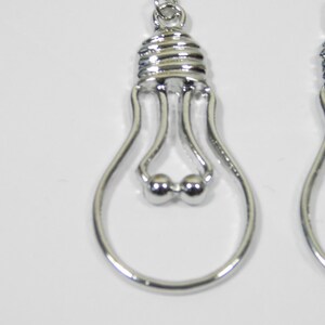 May include: A pair of silver lightbulb shaped dangle earrings. The earrings have a small silver ball at the top and a silver loop at the bottom.