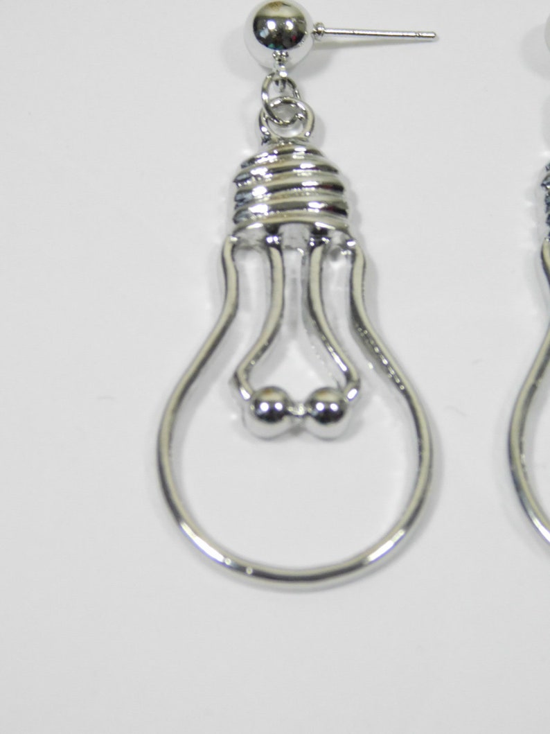May include: A pair of silver lightbulb shaped dangle earrings. The earrings have a small silver ball at the top and a silver loop at the bottom.