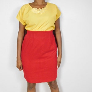 May include: A two-piece outfit featuring a yellow top and a red skirt. The top has short sleeves and a decorative floral applique at the neckline. The skirt is a solid red color and has a fitted silhouette.