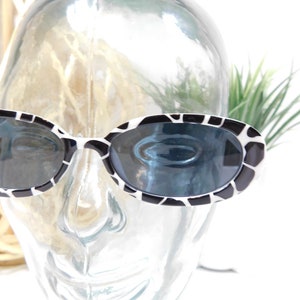 May include: Black and white oval sunglasses with a zebra print pattern. The sunglasses are on a mannequin head.