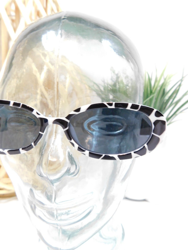 May include: Black and white oval sunglasses with a zebra print pattern. The sunglasses are on a mannequin head.