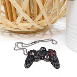 Könnte beinhalten: Eine schwarze und silberne Kettenkette mit einem schwarzen, diamantbesetzten Videospiel-Controller-Anhänger. Der Controller hat rote und grüne Akzente.