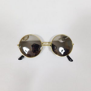 May include: Gold-rimmed round sunglasses with mirrored lenses. The lenses are reflective and show a blurry image of a person.