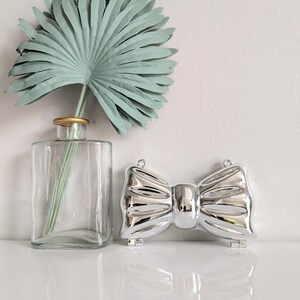 May include: A silver bow-shaped clutch purse with a shiny metallic finish. The purse is closed and has a hinged clasp.