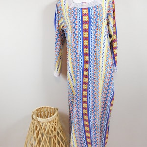 May include: A long, white dress with a blue, yellow, red and orange geometric pattern. The dress has a lace trim around the neckline and sleeves.