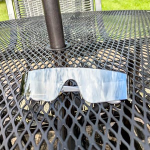 Puede incluir: Un par de gafas de sol transparentes y espejadas con un reflejo azul cielo. Las gafas de sol están sobre una mesa de metal negro.