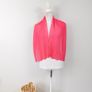 May include: A pink pleated scarf with a chevron pattern. The scarf is displayed on a white mannequin.