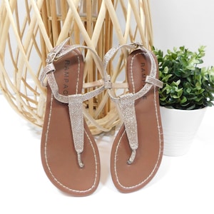 May include: A pair of gold glitter sandals with brown leather straps and soles. The sandals have the word "RAMPAGE" written on the straps.