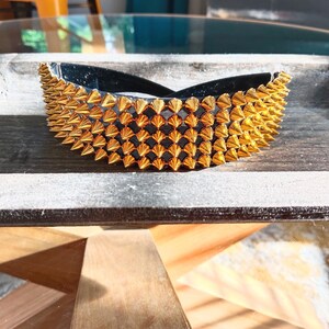May include: A black bowl with a gold-coloured, spiked trim. The bowl is on a wooden surface. The spikes are evenly spaced, creating a decorative border. The bowl is likely for holding small items. The bowl's dimensions are not visible.